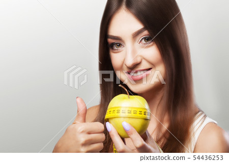 Diet. Sport. Young beautiful girl holds an apple and a measuring tape in her hands. Beautiful skin 54436253