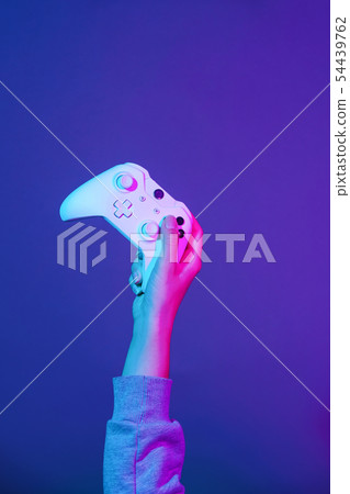 Hand with white gamepad on dark violet background. 54439762