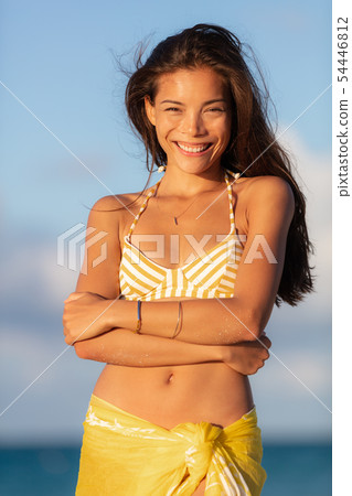 Beautiful Asian young woman wearing yellow bikini smiling candidly happy on summer travel beach 54446812