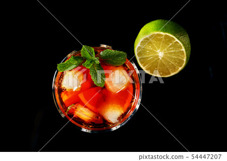 Glass of Dark Rum Cocktail with lime, orange, ice cubes and mint leaves on black mirror background 54447207