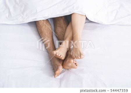 Male and female legs under duvet lying on bed Male and female legs under duvet lying on bed 54447359