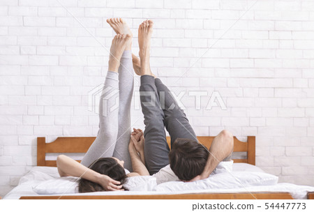 Young couple lying on bed and raising legs in air 54447773