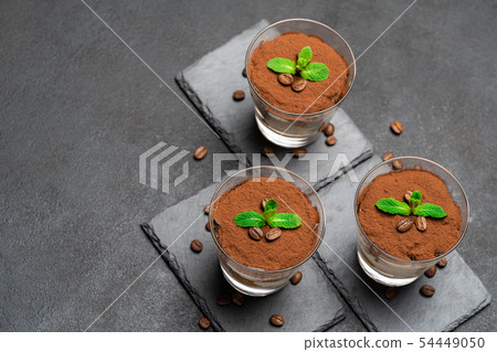 Classic tiramisu dessert in a glass on stone serving board on dark concrete background Classic tiramisu dessert in a glass on stone serving board on dark concrete background 54449050
