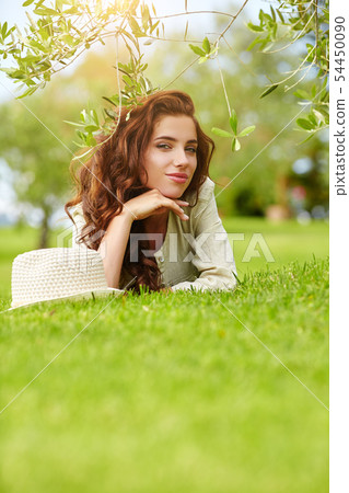 Beautiful smiling woman lying on a grass outdoor. 54450090