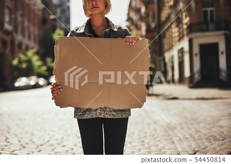Cropped photo of young woman holding a blank banner while standing on the empty road. 54450814