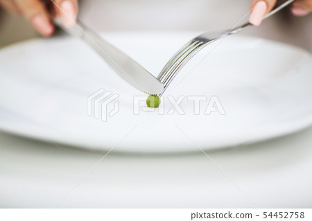 Eating disorder. Girl is holding a plate and trying to put a pea on the fork 54452758