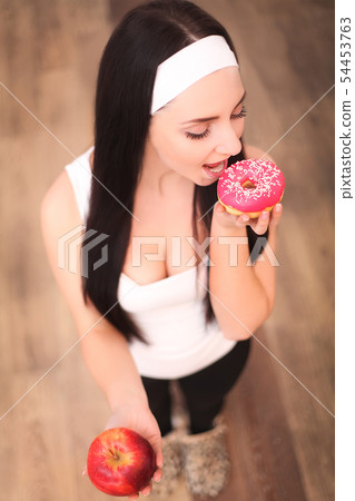 Beautiful young woman making choice between apple and donut, close up Beautiful young woman making choice between apple and donut, close up 54453763