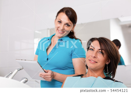 Dentist finishing successful teeth restoration, black haired doctor, in green mask, giving to happy Dentist finishing successful teeth restoration, black haired doctor, in green mask, giving to happy 54454121