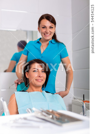Dentist finishing successful teeth restoration, black haired doctor, in green mask, giving to happy Dentist finishing successful teeth restoration, black haired doctor, in green mask, giving to happy 54454125