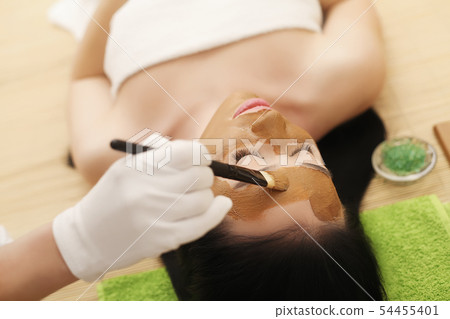Beauty procedures skin care concept. Young woman applying facial mud clay mask to her face Beauty procedures skin care concept. Young woman applying facial mud clay mask to her face 54455401