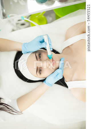 Doctor with Ultrasonic scraber. Doing procedure of ultrasonic cleaning of face. Model, profile Doctor with Ultrasonic scraber. Doing procedure of ultrasonic cleaning of face. Model, profile 54455521