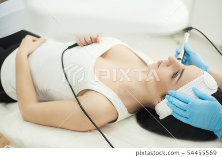 Doctor with Ultrasonic scraber. Doing procedure of ultrasonic cleaning of face. Model, profile Doctor with Ultrasonic scraber. Doing procedure of ultrasonic cleaning of face. Model, profile 54455569