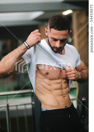 Young athlete posing with a torso for photography in gym. Bodybuilder, athlete with pumped muscles Young athlete posing with a torso for photography in gym. Bodybuilder, athlete with pumped muscles 54459975