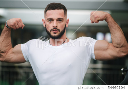 Young athlete posing with a torso for photography on a gym background. Bodybuilder, athlete with Young athlete posing with a torso for photography on a gym background. Bodybuilder, athlete with 54460104