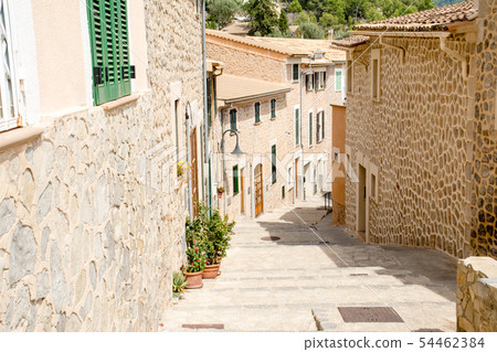 Majorca's cityscape A pale-marooned wall and stone-walled houses with windows with cobblestone alleys and plants with green dark doors 54462384