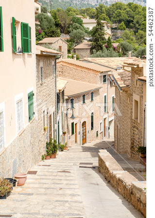 Majorca's cityscape A pale-marooned wall and stone-walled houses with windows with cobblestone alleys and plants with green dark doors 54462387