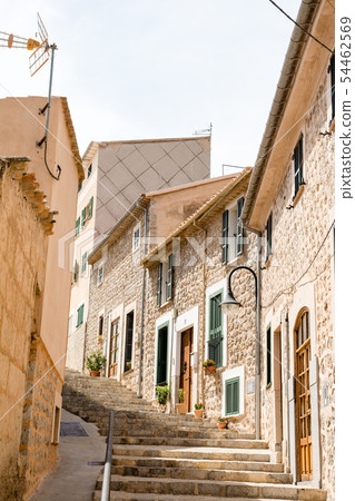Majorca's cityscape A pale-marooned wall and stone-walled houses with windows with cobblestone alleys and plants with green dark doors 54462569
