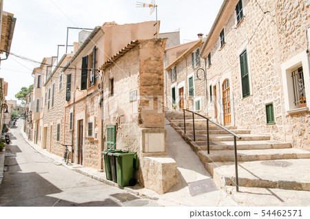 Majorca's cityscape A pale-marooned wall and stone-walled houses with windows with cobblestone alleys and plants with green dark doors 54462571