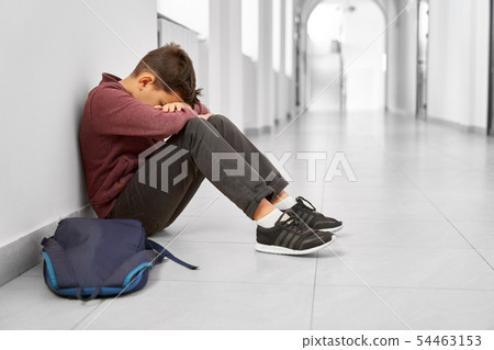Sad school boy sitting alone on floor at corridor. 54463153