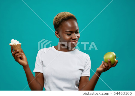 Girl in white shirt keeping healthy and unhealthy food 54463160
