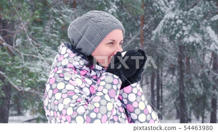 A female tourist stands against a winter forest or park on a snowy day and drinks hot tea from a cup A female tourist stands against a winter forest or park on a snowy day and drinks hot tea from a cup 54463980