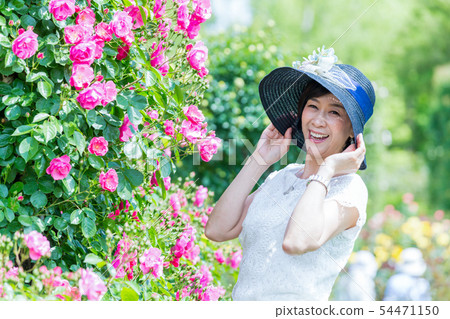 享用玫瑰園的中間婦女在盛開羅斯曲拱玫瑰園 享用玫瑰園的中間婦女在盛開羅斯曲拱玫瑰園 54471150