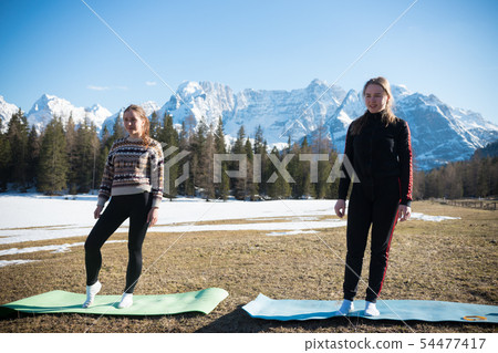 Dolomites - Two young women standing on yoga mats on a background of the forest 54477417