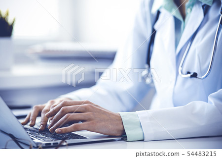 Doctor woman using laptop computer while sitting at the desk near window in hospital. Medicine and 54483215
