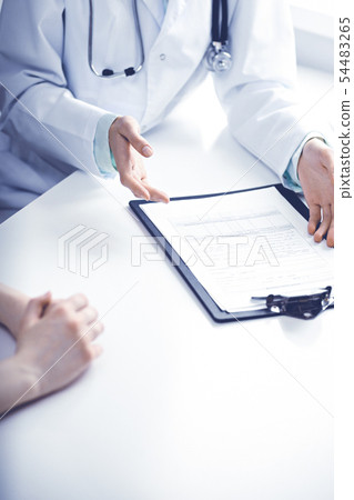 Doctor and female patient sitting at the desk and talking in clinic near window. Medicine and health 54483265
