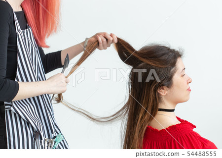 Hair Stylist, coloring and people concept - red hair hairdresser coloring young woman in red shirt 54488555