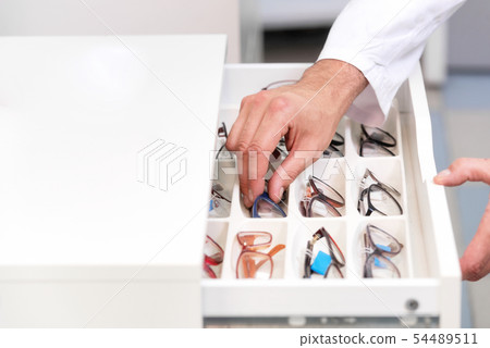 ophthalmologist hands close up, choosing glasses from a drawer in the optical store. 54489511