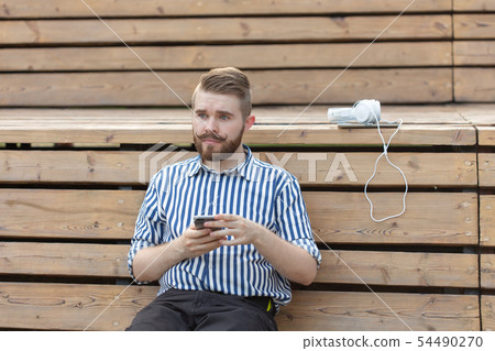 Pensive serious young male hipster student with a mustache and beard writing sms message to his 54490270