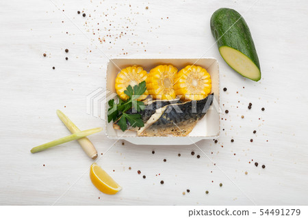 Top view slices of fish and boiled corn lie in the lunch box next to the zucchini leek and corn 54491279