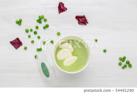 Cup of green soup with pieces of vegetables is on a white table with green peas. Healthy eating Cup of green soup with pieces of vegetables is on a white table with green peas. Healthy eating 54491290