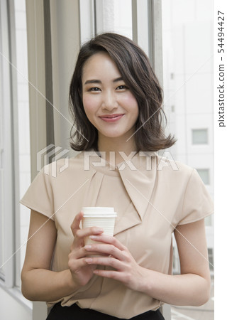 拿著飲料的微笑的婦女在辦公室 拿著飲料的微笑的婦女在辦公室 54494427