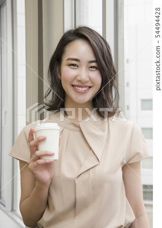 拿著飲料的微笑的婦女在辦公室 拿著飲料的微笑的婦女在辦公室 54494428