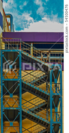 An tall concrete apartment block with repeating external fire escape stairs with metal railings and 54500476