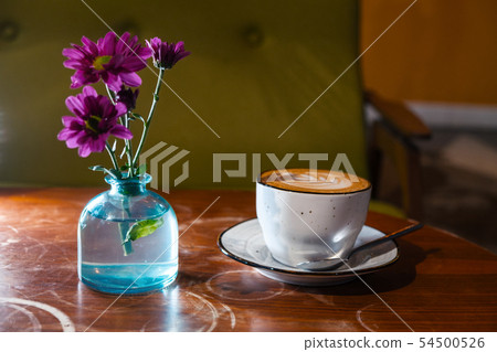 Cappuccino cup on table wih flowers in bottle 54500526
