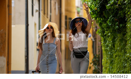 Two young women walking though the streets and talking. Two young women walking though the streets and talking. 54508412