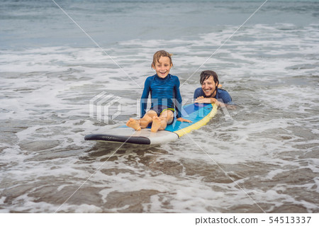 Father or instructor teaching his 5 year old son how to surf in the sea on vacation or holiday 54513337