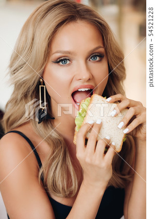 Attractive woman eating delicious sandwich in cafe 54521228