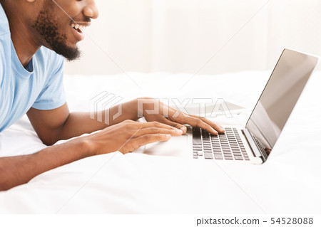 Black man blogger typing on laptop in bed 54528088
