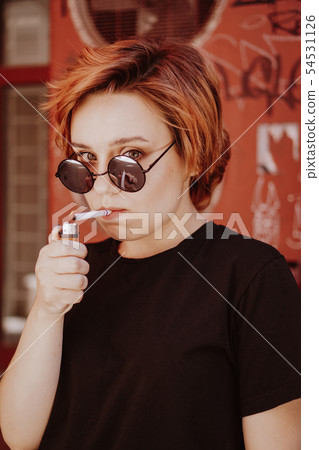 Millennial girl with short red hair and mirror sunglasses smoking cigarette 54531126