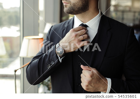 a man in a black suit straightens his tie 54535601