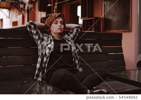 Young woman with short red hair in a bar put her legs on the bench Young woman with short red hair in a bar put her legs on the bench 54549092