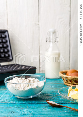 Making waffles at home - waffle iron and ingredients - milk, eggs and flour. Making waffles at home - waffle iron and ingredients - milk, eggs and flour. 54550590