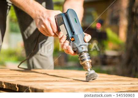 Hands man with electrical rotating brush metal disk sanding a piece of wood 54550903