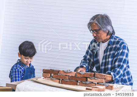 Little boy is learning how to build brick wall 54559933