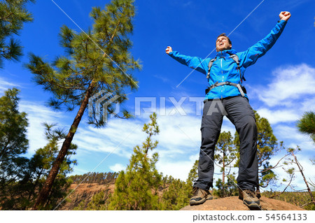Man hiking reaching summit top cheering in forest 54564133