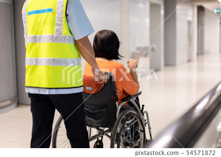 Caretaker push elderly woman on wheelchair in airport terminal. Caretaker push elderly woman on wheelchair in airport terminal. 54571872